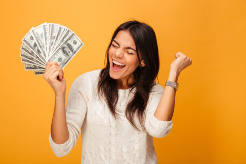 Excited lady with a fan of money in front of a bright orange background 