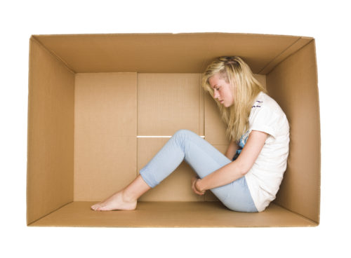 Sad girl sitting in a cardboard box 