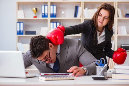 Young professional woman with boxing gloves punching young professional man