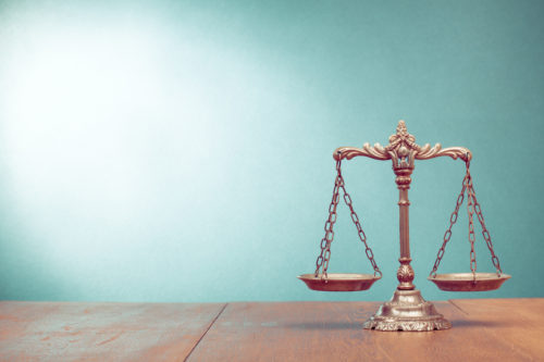 Scales of justice on table with solid teal background 
