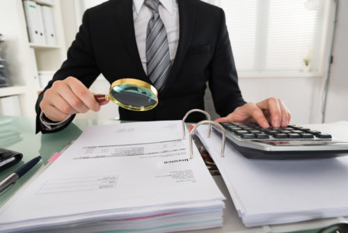 Professional man going over legal paperwork with a magnifying glass and a calculator 