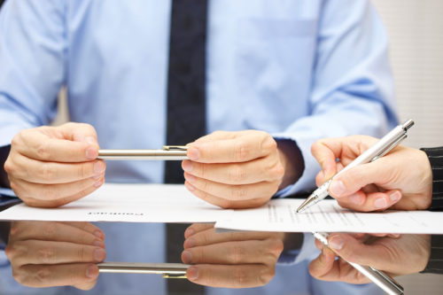 Men signing paperwork with silver pens