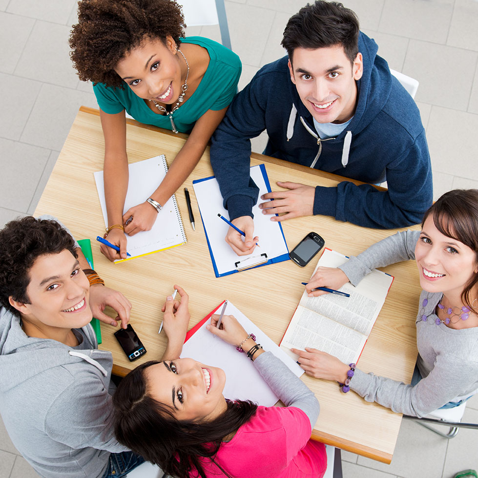 Young group of people sitting at a table with books and paperwork looking up to smile