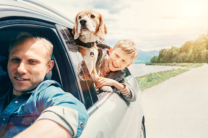 Man driving with child's head and dog both poking out of the window.