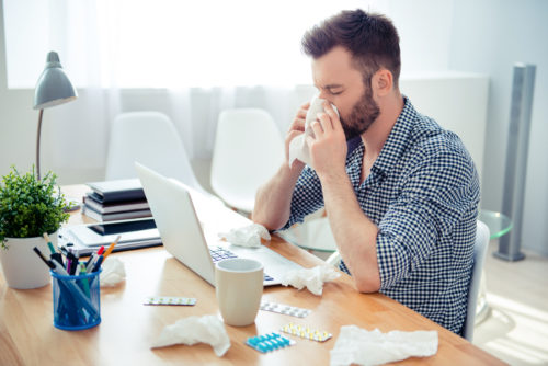 Casual dressed young man blowing his nose at his desk