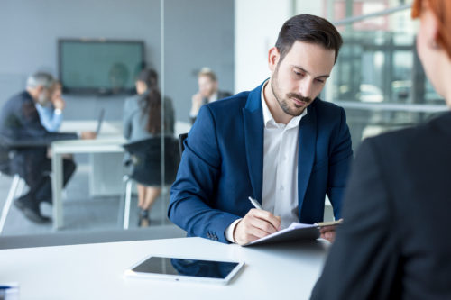 Professional man signing papers while a business meeting is going on in the background 