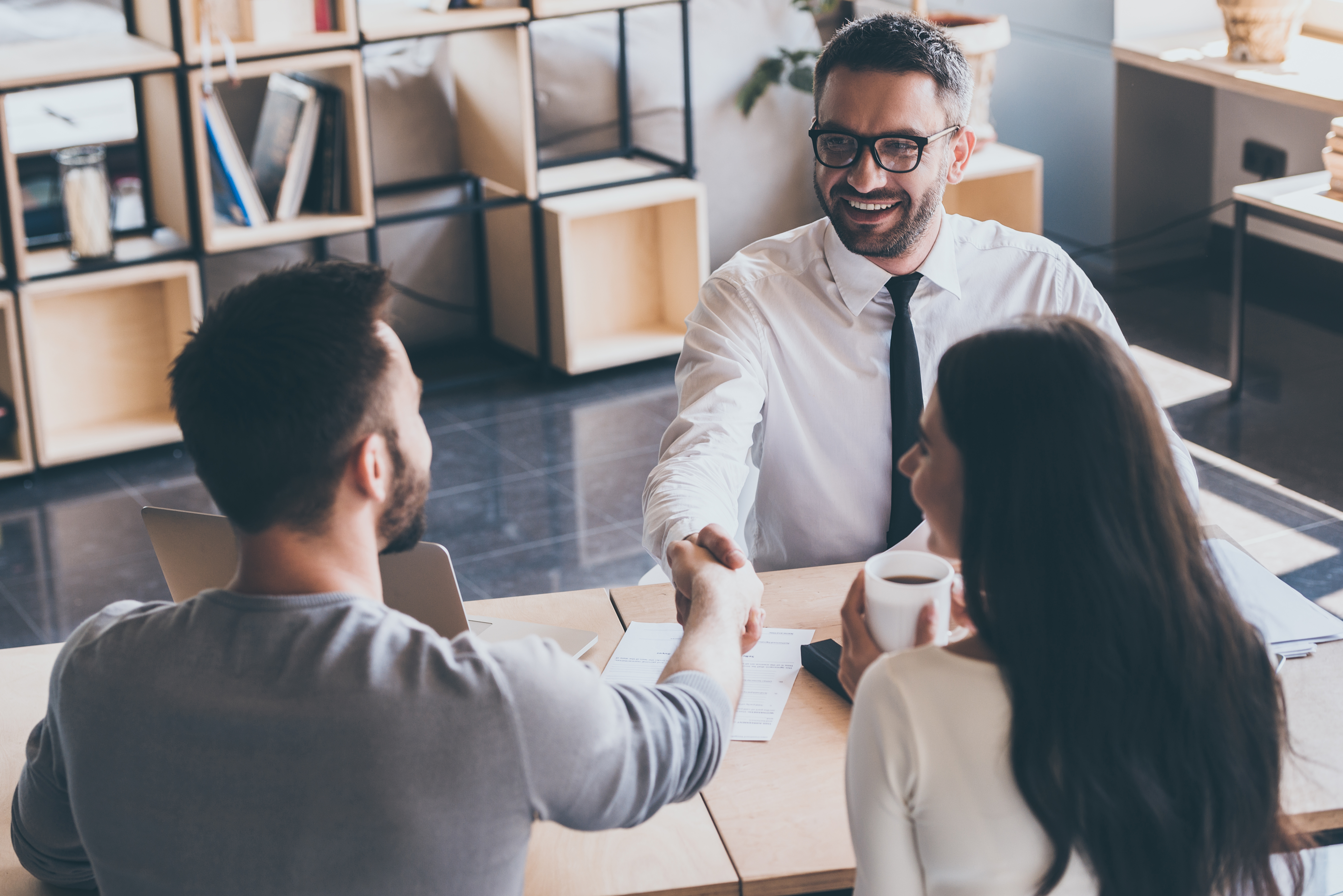 Professional men shaking hands at a table with lady sitting next to them 