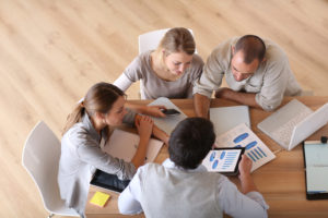 Four professionals sitting at a table with notes and technology 