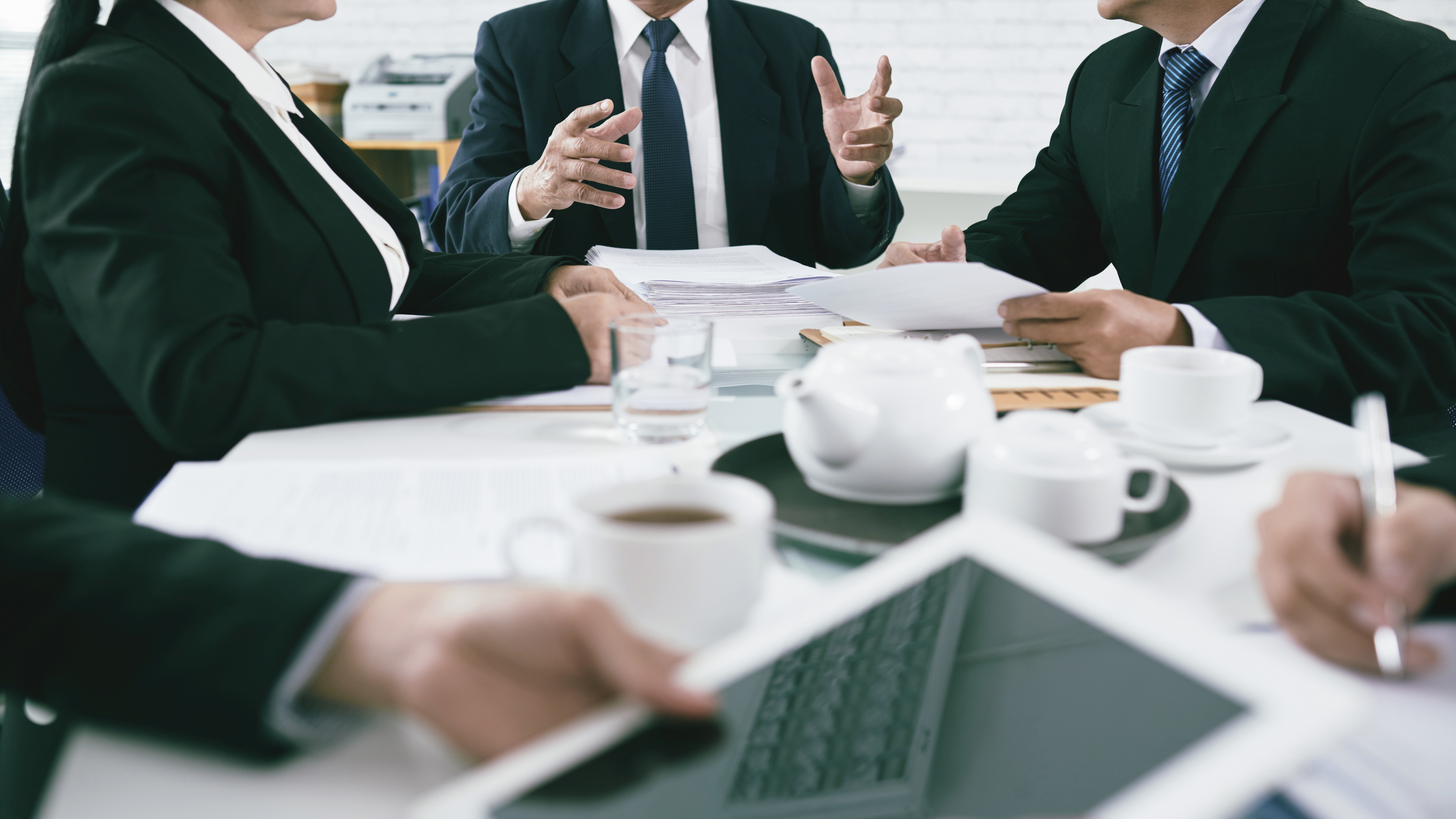 Professional men sitting at a table discussing business with a teapot in the center 