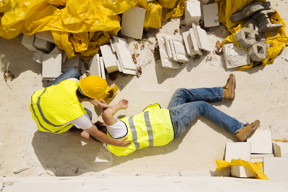 Man hurt at construction site with other worker kneeling over him trying to help